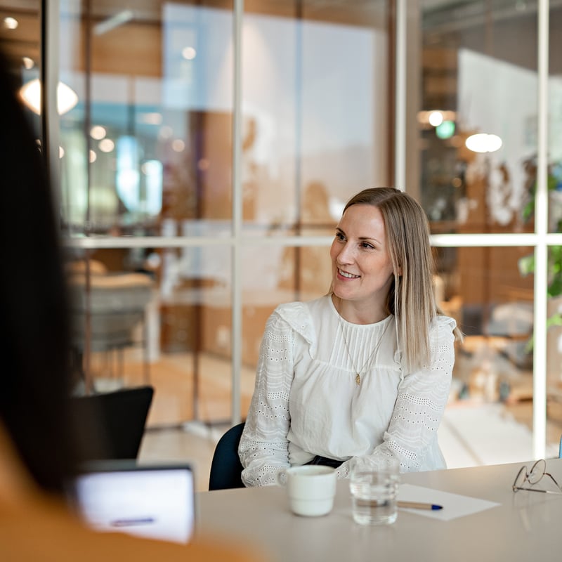 Bilde av en dame med hvit skjorte som sitter og smiler