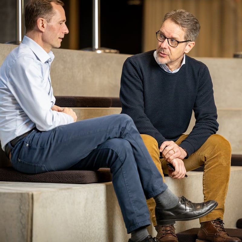 To menn sitter på en betongtrapp og snakker med hverandre