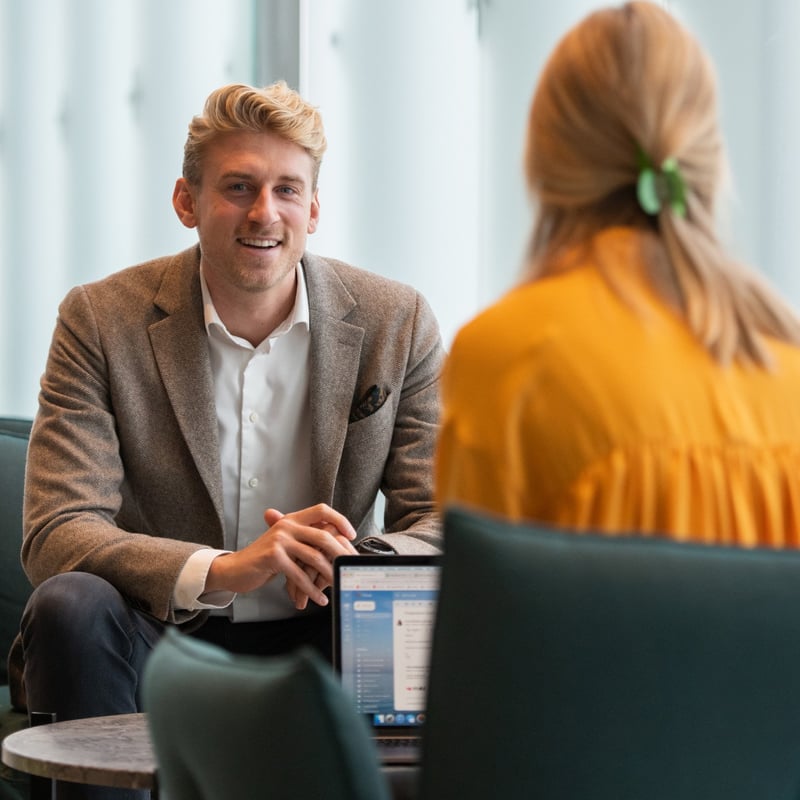 Mann med dressjakke sitter og smiler mot kamera