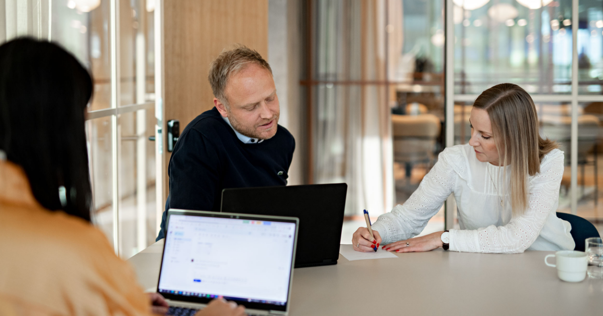 Tre personer sitter rundt et bord og prater