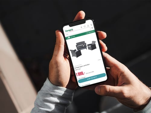En sofagruppe på europris.no vises på en mobil som holdes i to hender