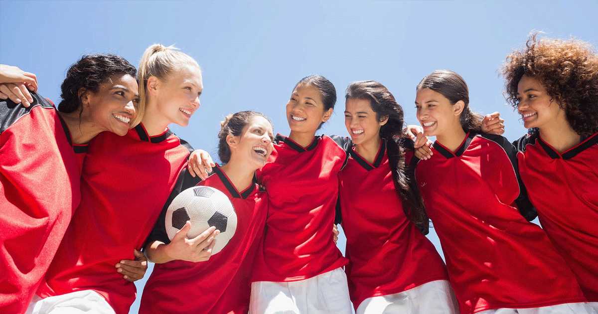 En gjeng med jente ri fotballdrakt holder rundt hverandre og smiler