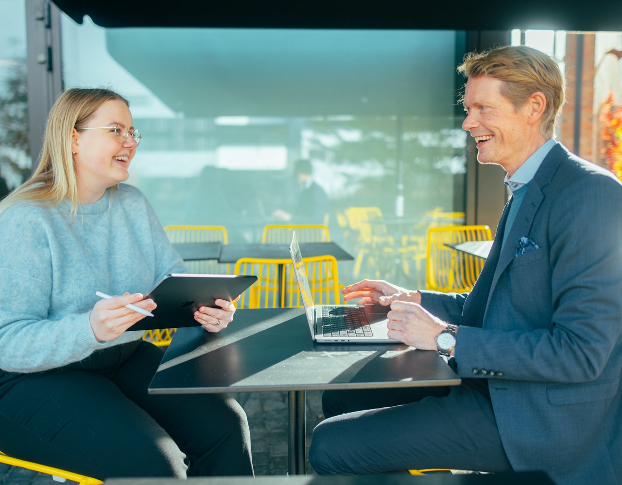 En mann og en dame sitter på en kafe og prater mens de jobber med process mining