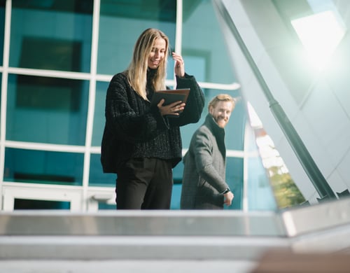 Bilde av en dame med en ipad i hånen og en mann i bakgrunn