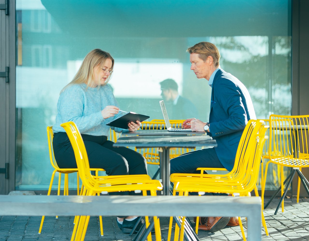 En dame og en mann sitter på en kafe med gule stoler og jobber