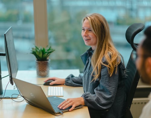 Ung dame jobber på en PC mens hun smiler og ler