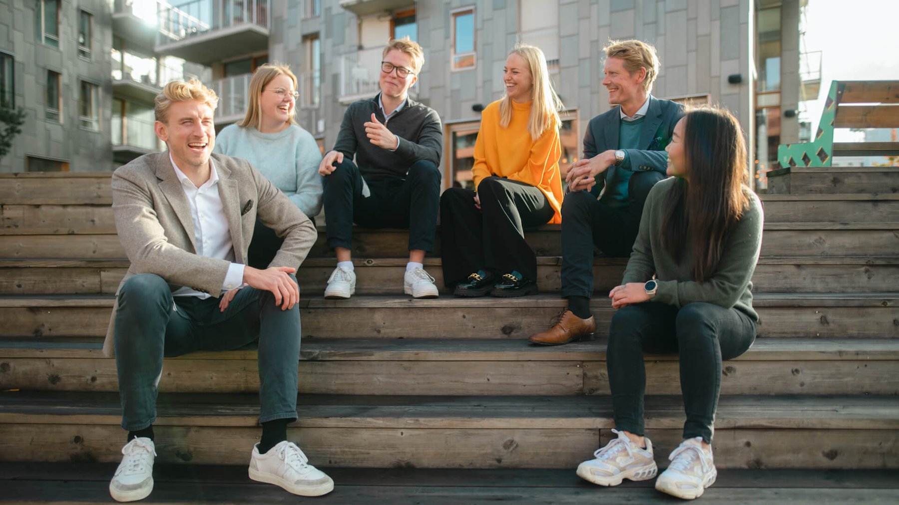 En gruppe mennesker sitter ute i en trapp og ler og smiler