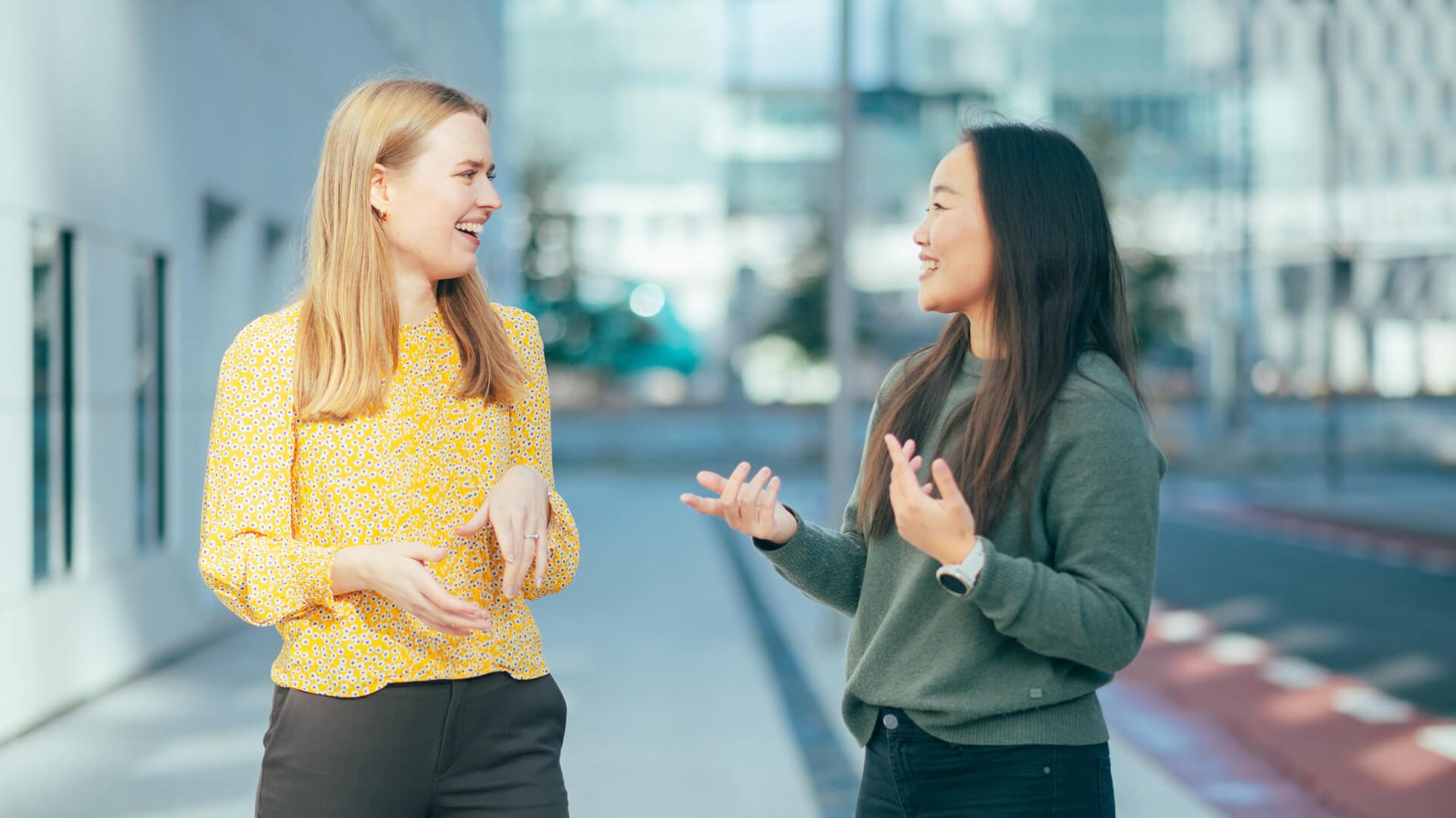 To damer står og prater utendørs sammen mens de smiler til hverandre