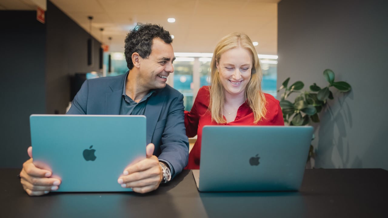 Mann og dame sitter foran hver sin PC og smiler