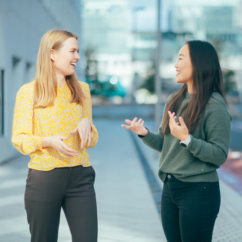 To damer står og prater utendørs sammen mens de smiler til hverandre