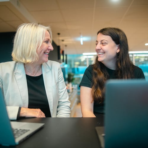 To kvinnelige kollegaer sitter sammen og smiler