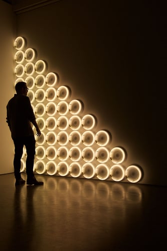 Et menneske står og ser på lysende lamper festet i vegg