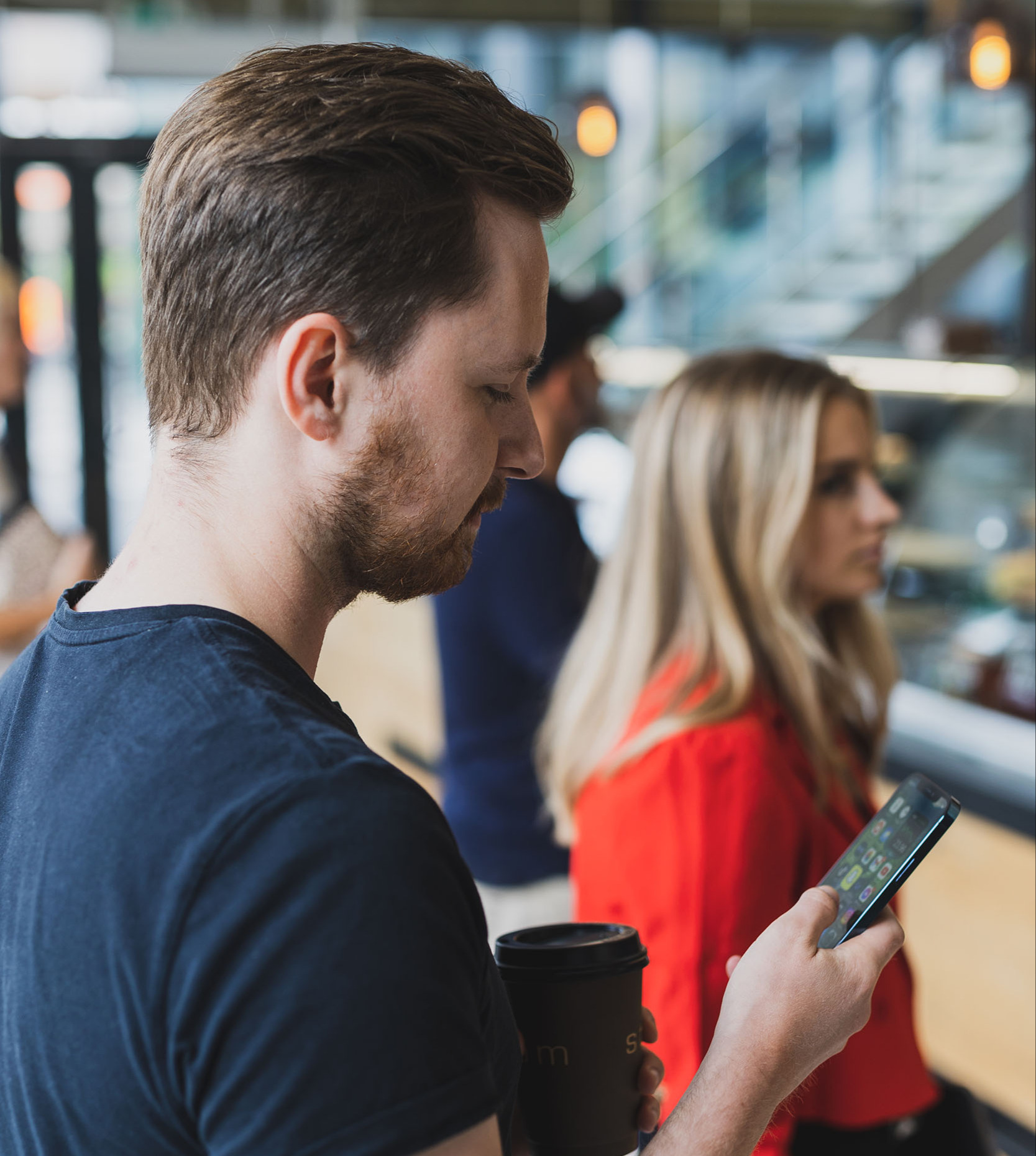 man looking at his phone, and a blond girl in the background