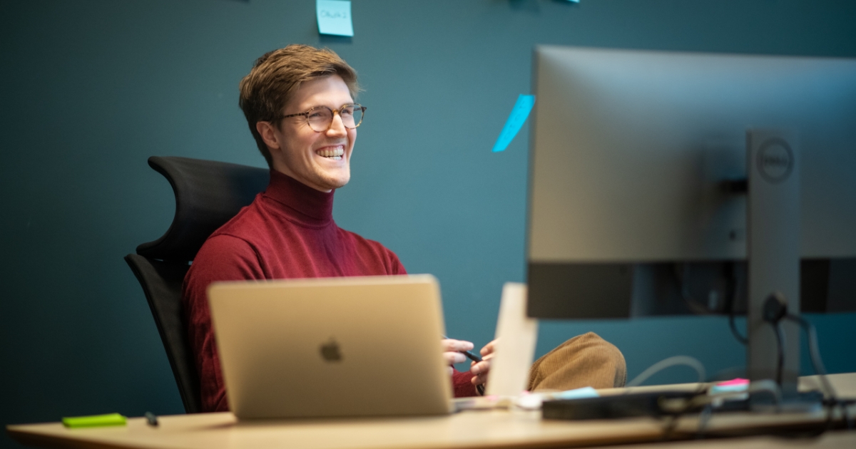 Mann sitter foran en PC og smiler