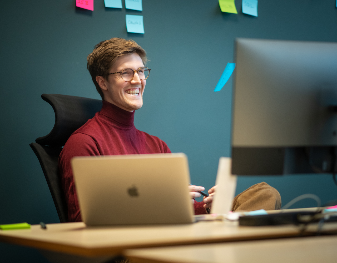 Mann sitter bak en PC-skjerm og smiler